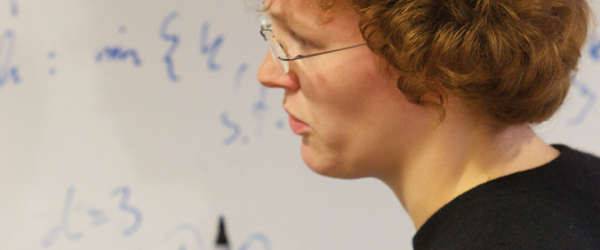 A student with glasses looking at a whiteboard showing mathematical symbols
