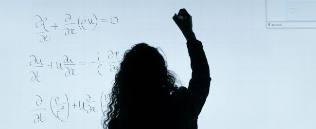 A woman writing maths equations on a whiteboard