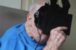 An elderly man hold a piece of headset technology to his face