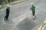 two children running around playing joyfully on a closed street, with chalk drawings on the ground.