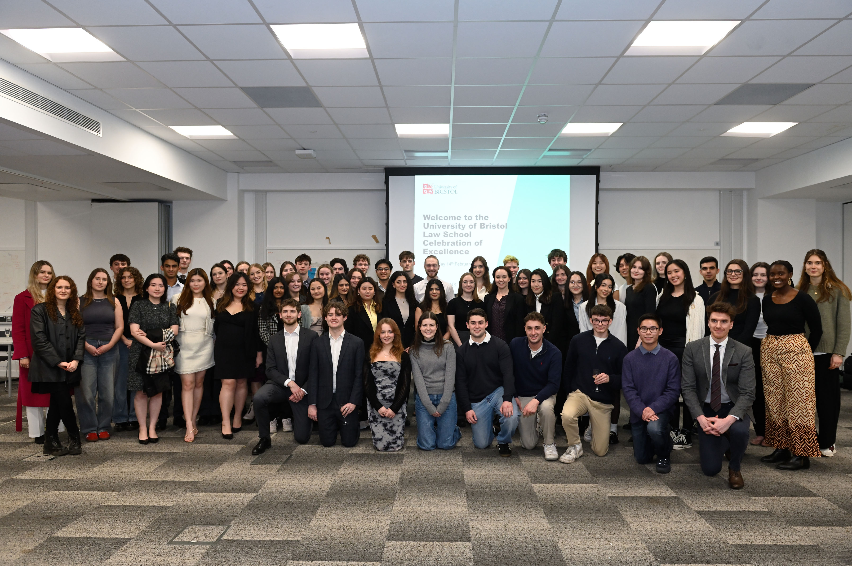 large group shot of law student prize winners, smiling looking at the camera, wearing smart clothes in an teaching room setting.