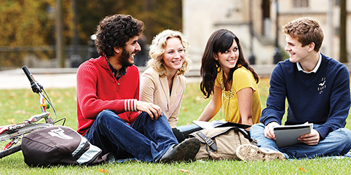 A racially diverse group of two men and two women, sitting together in a green space and smiling.