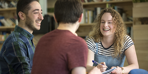Three students laugh while having a conversation in a study space.